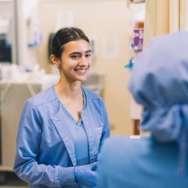 Nursing student in blue scrubs smiling during a simulation lab.
