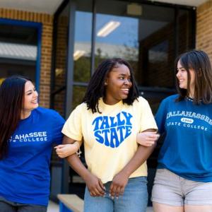 Three students walking with their arms linked.