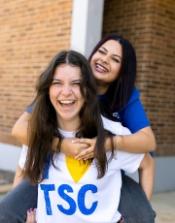 TSC student laughing while carrying another student on their back.