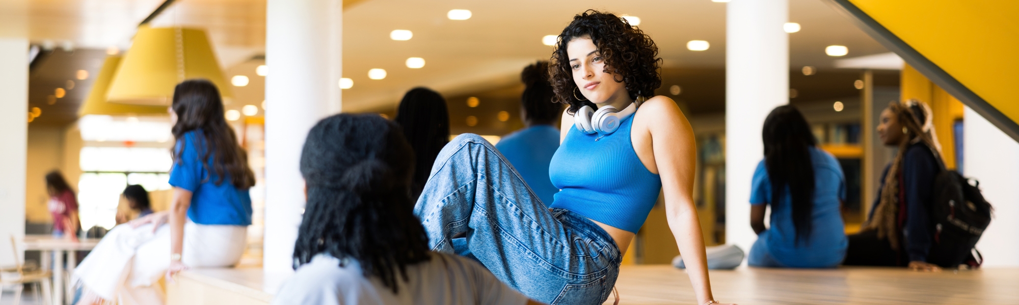 Student sitting underneath yellow stairwell listening to friend talk.
